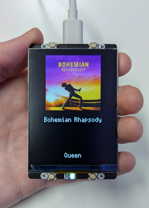 Hand holding Pico with a display showing the cover art, song name and artist of Bohemian Rhapsody by Queen